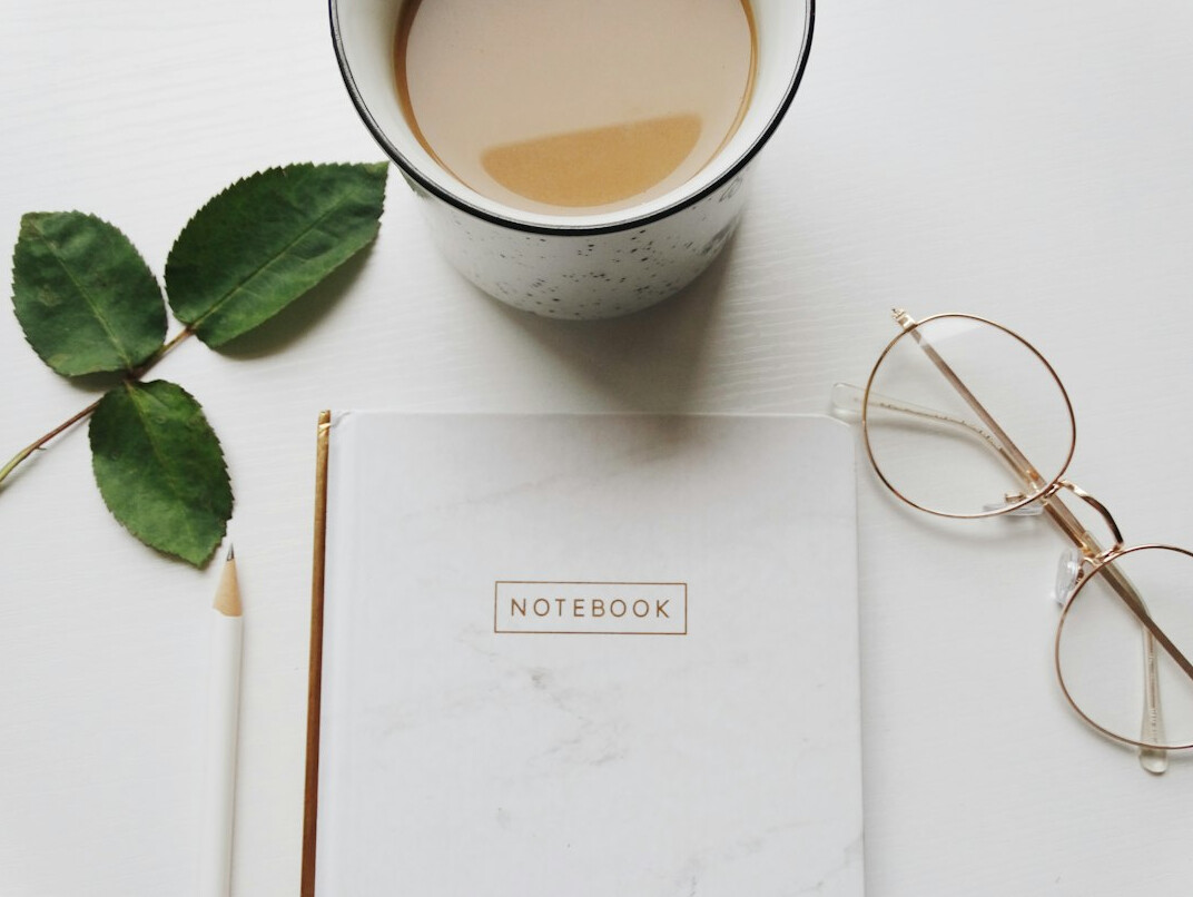 Overhead flat lay of a desk with a laptop, notebook and coffee cup